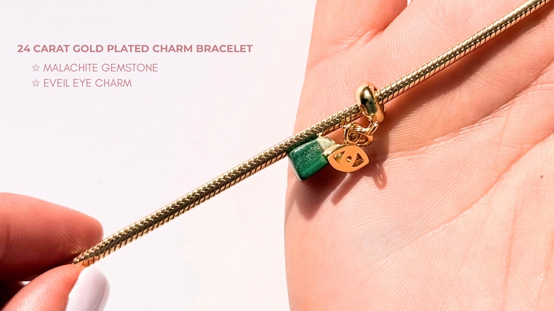 Gold-plated charm bracelet with malachite gemstone and evil eye charm held in hand against a white background.